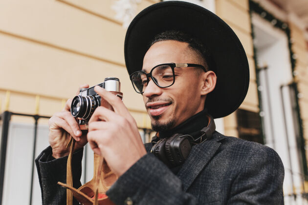 城市快乐的男性摄影师 棕色皮肤 早上在户外工作照片中 积极的非洲男人穿着深色衣服 拿着相机站在街上自信休闲黑发