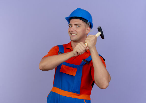 肩膀面带微笑的年轻男性建筑工人身穿制服 头戴安全帽 肩上扛着锤子就紫了头盔年轻微笑