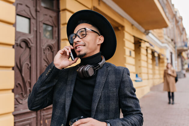 时尚快乐的美国男人穿着时髦的灰色衣服 站在老建筑附近打电话热情的非洲男人打电话给某人 面带微笑白天手机享受