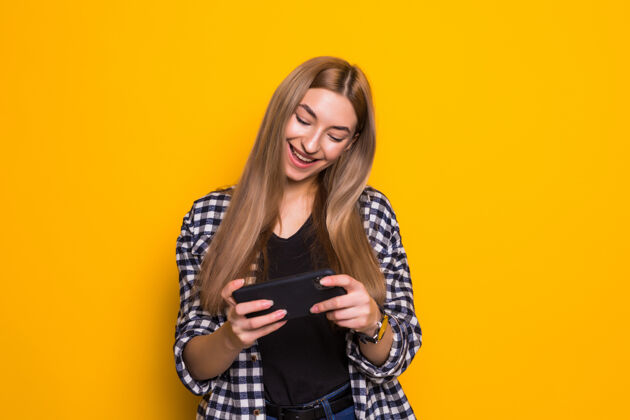 女性快乐可爱的年轻女子玩手机游戏的画面隔着黄色的墙看向一边姿势可爱旁白