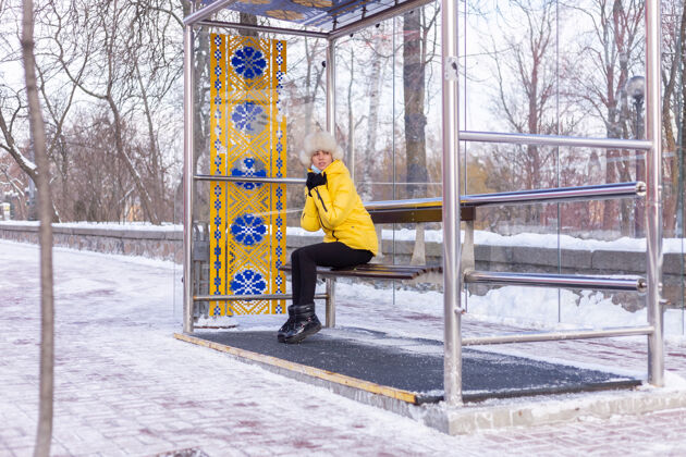 乘客在寒冷的日子里 一个穿着冬衣的女人在公共汽车站等公共汽车围巾城镇肖像