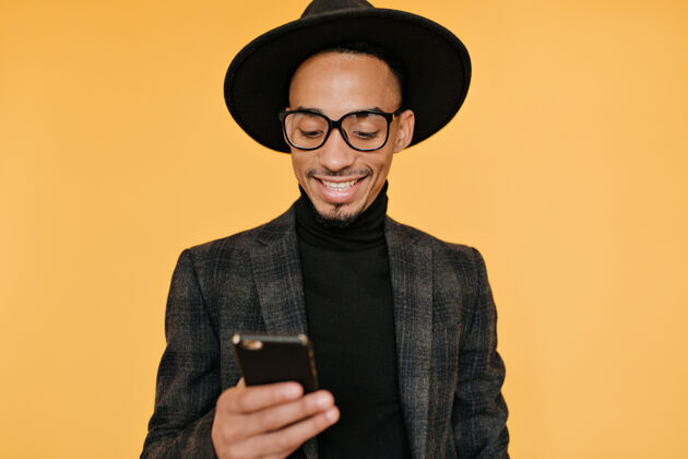 时尚令人惊奇的留着胡须的非洲男人在发短信高兴的混血男模微笑着看着他的手机套装帅气男士