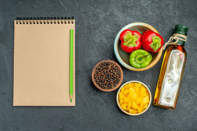 盘子顶视图的甜椒碗在右侧与草药和蔬菜碗油瓶和记事本在一边的绿色桌子上油午餐草药