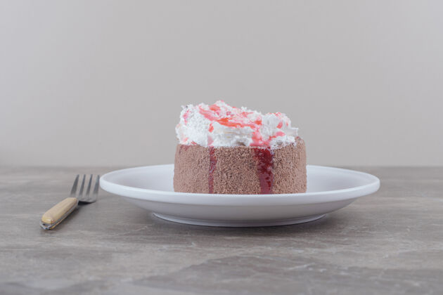 盘子一个小蛋糕 上面放着奶油和草莓糖浆 放在大理石盘子上美味糕点甜点