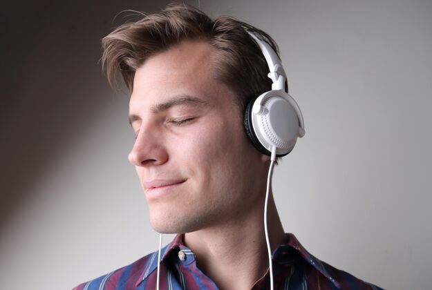肖像年轻的男人在灰色的墙上戴着耳机听音乐声音音频娱乐