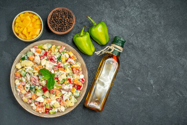 铃铛一碗蔬菜沙拉的俯视图 灰色背景上有一碗蔬菜和胡椒油瓶以及甜椒蔬菜背景碗
