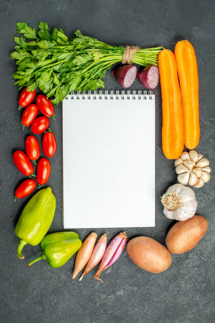 沙拉在深灰色背景上 笔记本的顶视图周围有蔬菜深色背景胡椒