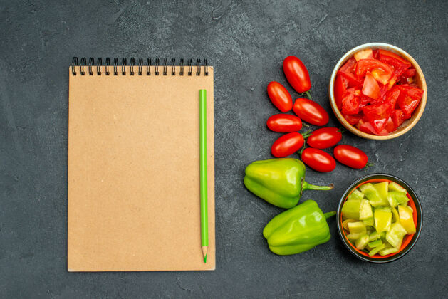 甜椒在深绿色的背景上 一碗碗甜椒和西红柿以及蔬菜和记事本的俯视图素食壁板新鲜