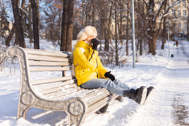 女士冬天的快乐年轻女子 穿着暖和的衣服 在阳光明媚的日子里 坐在长椅上 独自享受着新鲜的空气和咖啡快乐雪衣服