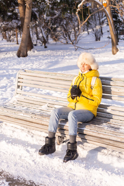 咖啡冬天的快乐年轻女子 穿着暖和的衣服 在阳光明媚的日子里 坐在长椅上 独自享受着新鲜的空气和咖啡女季节微笑