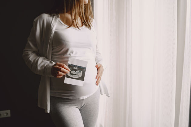 健康孕妇站在窗边看照片怀孕怀孕护理