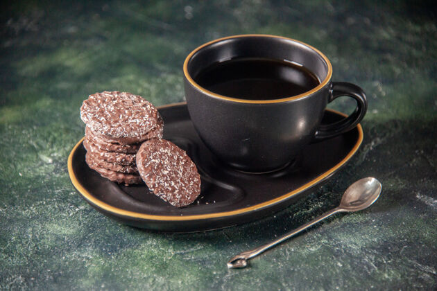 茶前视一杯红茶 茶杯和盘子上放着饼干 深色的表面上放着糖 仪式上放着玻璃早餐 甜点 彩色蛋糕杯子饼干糖