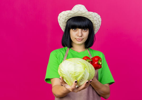 年轻自信的年轻女园丁穿着制服 戴着园艺帽 手里拿着卷心菜和红辣椒空间花园卷心菜