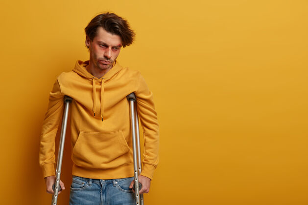 受伤脸受伤的失意男子拄着拐杖又学会走路了残疾运动衫骨折