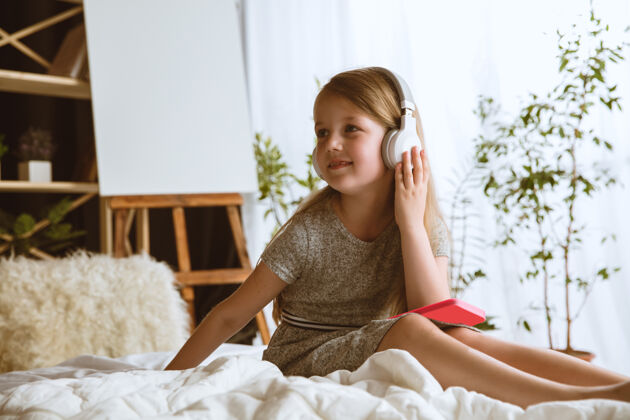 持有小女孩带着大耳机坐在床上听最喜欢的音乐 尽情享受耳机人脸