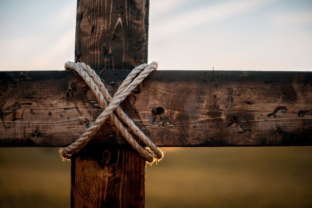风景一个木制十字架的特写镜头 周围缠着绳子 背景模糊河流电缆旧
