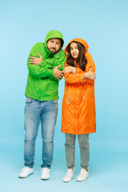 季节这对穿着秋夹克的年轻情侣在摄影棚里摆出蓝色的姿势人类的负面情绪寒冷天气的概念女性和男性的时尚概念寒冷外套凉爽