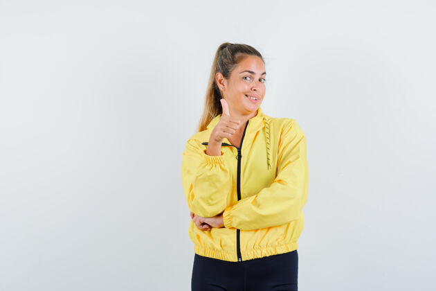 年轻一个金发女人 穿着黄色棒球服和黑色裤子 大拇指朝上 看上去很乐观向上乐观拇指
