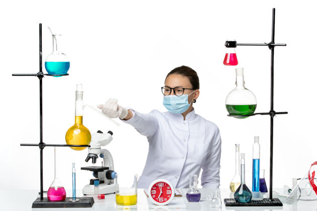 化学前视图穿着医疗服的女化学家戴着面罩坐在浅白色的背景上 化学实验室的病毒冠状病毒-飞溅实验实验室飞溅