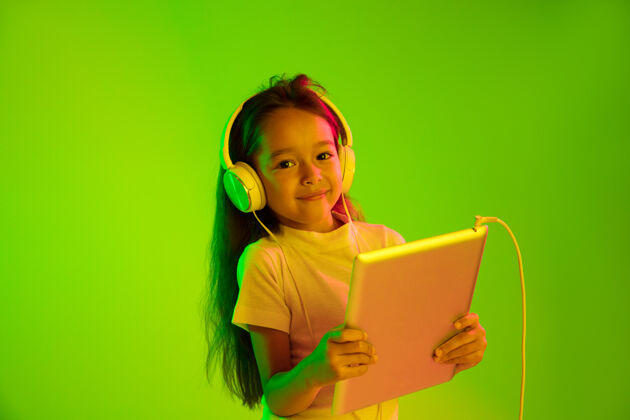 耳机美丽的女性半身像 隔离在霓虹灯下的绿色背景上年轻感性的女孩人类情感 面部表情概念时尚的颜色使用平板电脑进行游戏 虚拟博客 自拍女学生孩子海洋