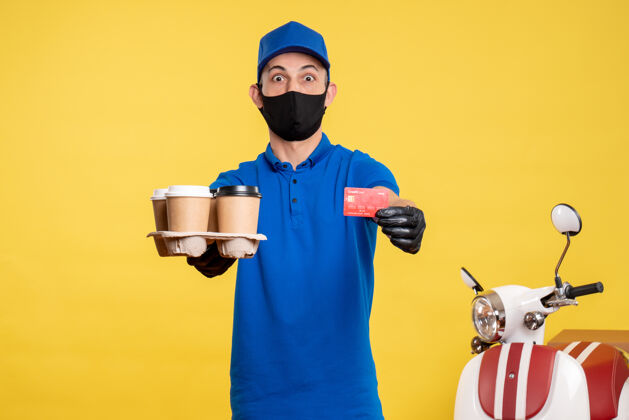 人正面图：戴着面具的男信使手拿咖啡和银行卡 穿着黄色工作服-投递服务男人黄色送货