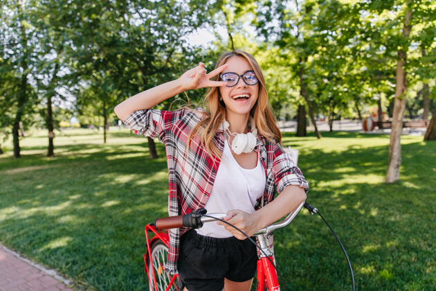 可爱时尚积极的女孩在夏日公园表达快乐穿着红衬衫的幸福女士与自行车合影的户外肖像风景快乐欧洲人
