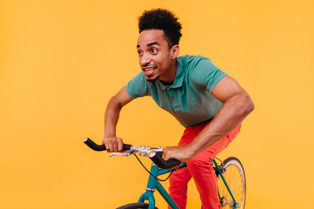 夏天一个穿着绿色t恤的黑眼睛年轻人骑着自行车一个穿着休闲装的快乐的非洲男人坐在自行车上活跃活动时髦