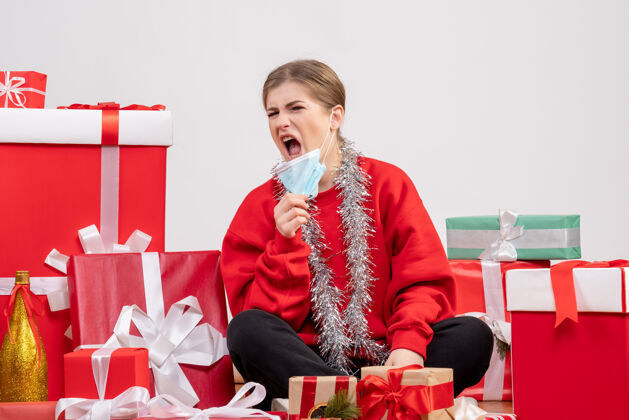 病毒正面图：年轻女性戴着无菌面具围坐在圣诞礼物旁人情绪现在