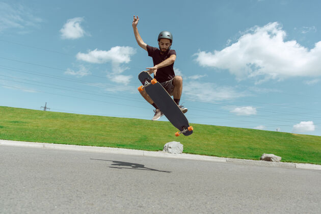 运动在阳光明媚的日子里 在城市街道上玩滑板的人年轻人在草地附近骑马 玩长板休闲活动 运动 极限 爱好和运动的概念滑板运动员男性