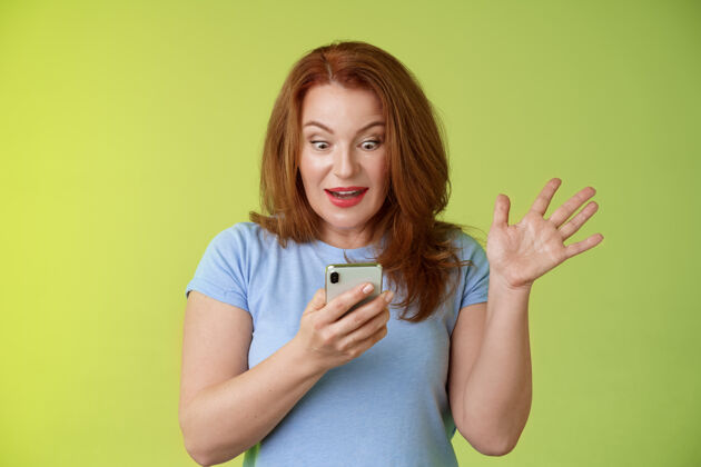 成熟惊喜热情快乐红发成熟中年女性收到精彩短信阅读完美新闻社交媒体手持智能手机凝视惊喜手机屏幕举手致胜满意印象成人