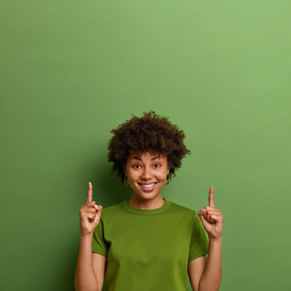 成人正面深色皮肤的女人在上面展示复制空间 食指向上 展示好 建议好主意 隔离在绿色墙壁上人和推广概念垂直积极牙齿
