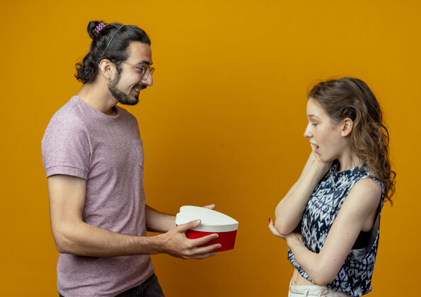 年轻人男人送礼物盒给他的女朋友 年轻漂亮的夫妇男人和女人在橙色的背景情侣礼物礼物