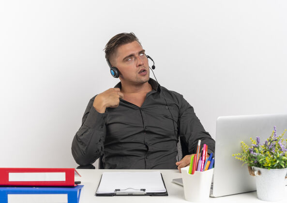 办公室年轻恼怒的金发上班族戴着耳机坐在办公桌旁 拿着办公工具 用笔记本电脑转动眼睛 把衣领隔离在白色背景上 留着复印空间工具衣领耳机