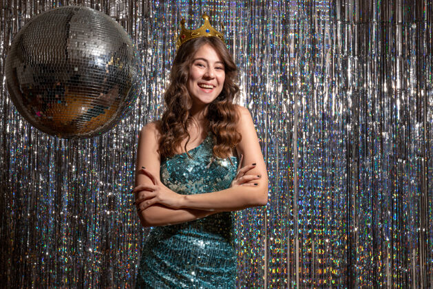 成人年轻的微笑积极迷人的女士穿着蓝绿色闪亮的礼服与亮片皇冠在聚会上穿着喷泉漂亮