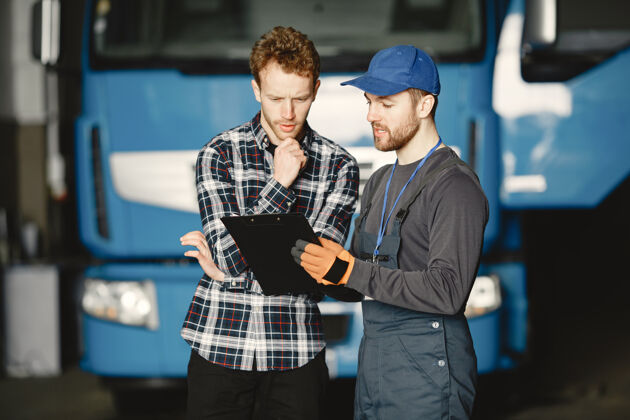卡车两个家伙在谈论工作在卡车附近的车库工作用货物转移文件年轻人卷发修理工