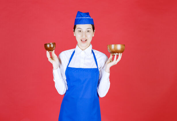 年轻穿着蓝色围裙的厨师双手捧着两个陶制的中国茶杯铜模特服装
