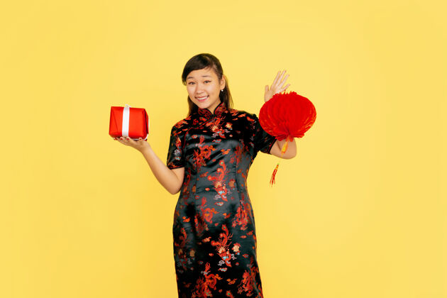 年带着灯笼和礼物摆姿势 微笑着2020年中国新年快乐黄色背景上的亚洲少女肖像穿着传统服装的女模特看起来很快乐庆祝 情感复制空间青少年旗袍肖像