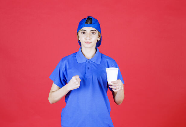 强壮身着蓝色制服的女服务人员手持一杯一次性饮料 露出拳头塑料人类年轻