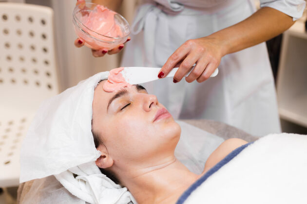 服务美容师用抹刀在女人脸上敷海藻酸钠面膜沙龙皮肤健康