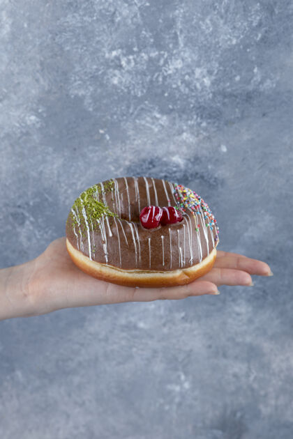 食物女性手拿美味的巧克力在大理石表面撒甜甜圈洒霜糕点