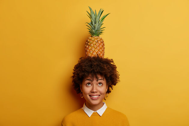 食物坚持住 不要摔倒幽默搞笑的黑皮肤女孩试图把菠萝放在头上 注意力集中在上面无忧无虑单色牙齿