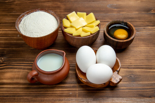 蜡烛正面图：棕色木制桌上全生鸡蛋加乳酪粉和牛奶产品蛋面团糕点生的糕点杯子