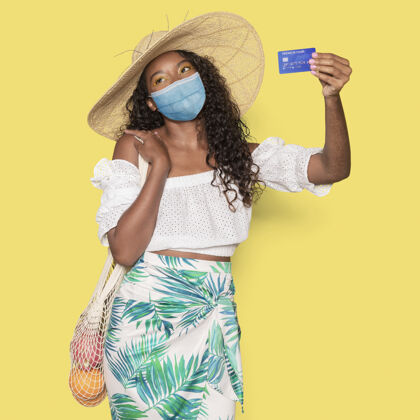 购物Covid19 戴着医用面具的女人拿着信用卡享受非洲帽子