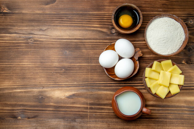 奶酪俯视整个生鸡蛋与面粉牛奶和奶酪在棕色的桌子上鸡蛋面团面粉粉粉粉产品颜色视图面粉