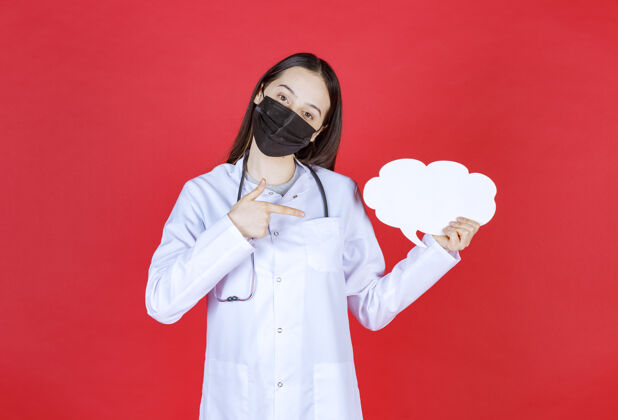 疾病女医生带着听诊器 戴着黑色面罩 手里拿着一张云状的空白问讯台健康指南病毒