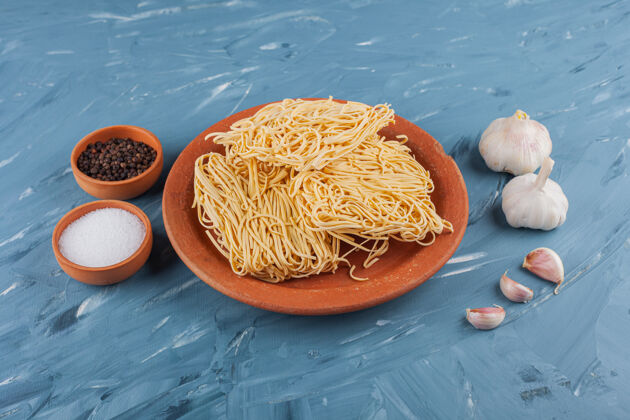 快速生方便面配上新鲜的大蒜素和香料放在蓝色的桌子上生的即食黄色