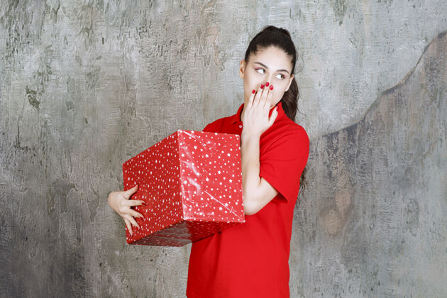 思考年轻女子拿着一个红色的礼品盒 上面有白点 看起来很体贴不确定成年人姿势