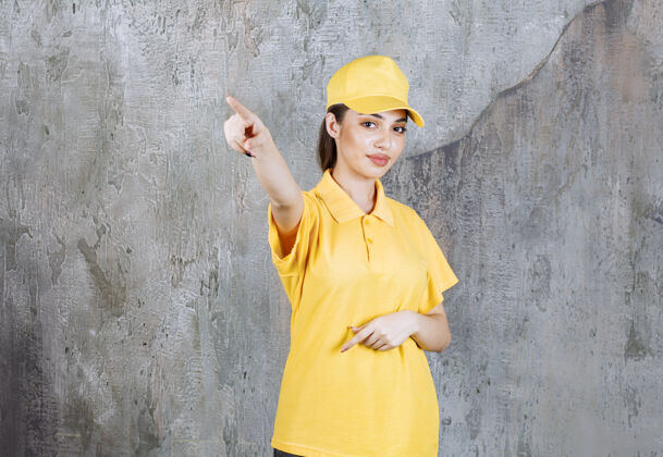 雇员身着黄色制服的女服务人员站在水泥墙上 展示左侧人员介绍信使