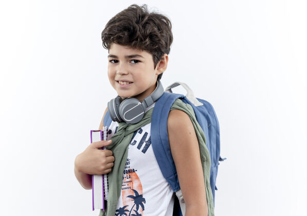 抱着看着镜头 戴着书包 戴着耳机 手里拿着一本书的小男孩高兴极了小学生请戴上背