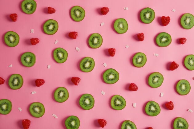 顶部绿色奇异果片 新鲜覆盆子和椰子片在粉红色工作室背景上分离营养食品概念由多汁水果制成的成分夏季 健康成分切块异国情调橘子